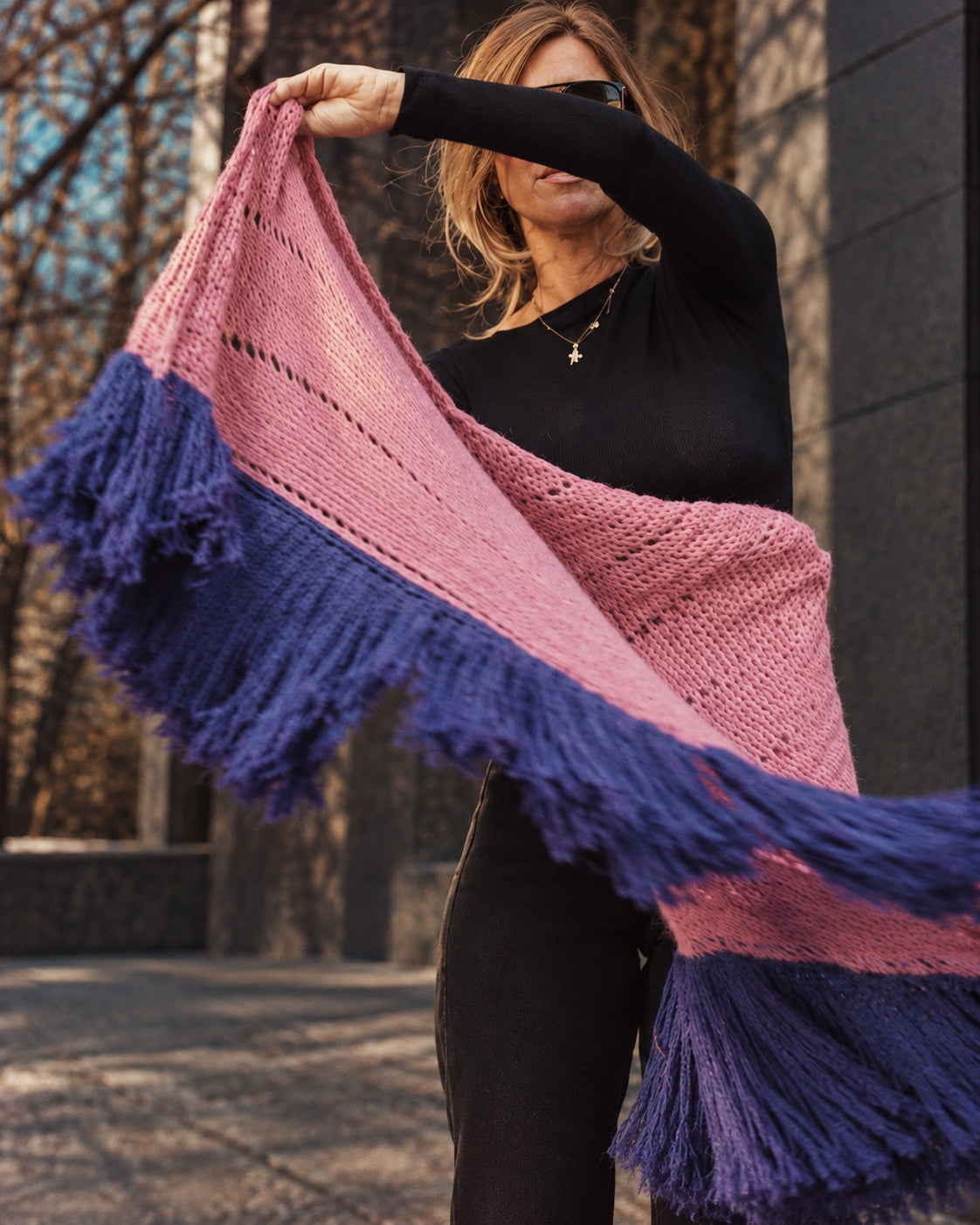 Donna vestita di nero apre lo scialle Odette rosa con lunghe frange viola in un cortile soleggiato