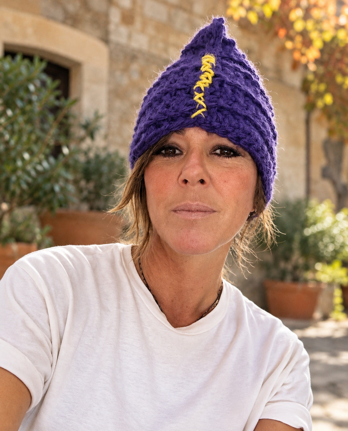 Donna in maglietta bianca indossa il berretto Kitri viola con cucitura gialla sul davanti